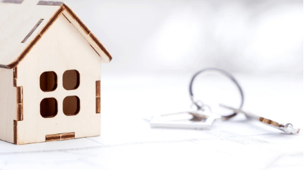 Wooden house model with keys, resting on a white surface, suggesting home ownership.