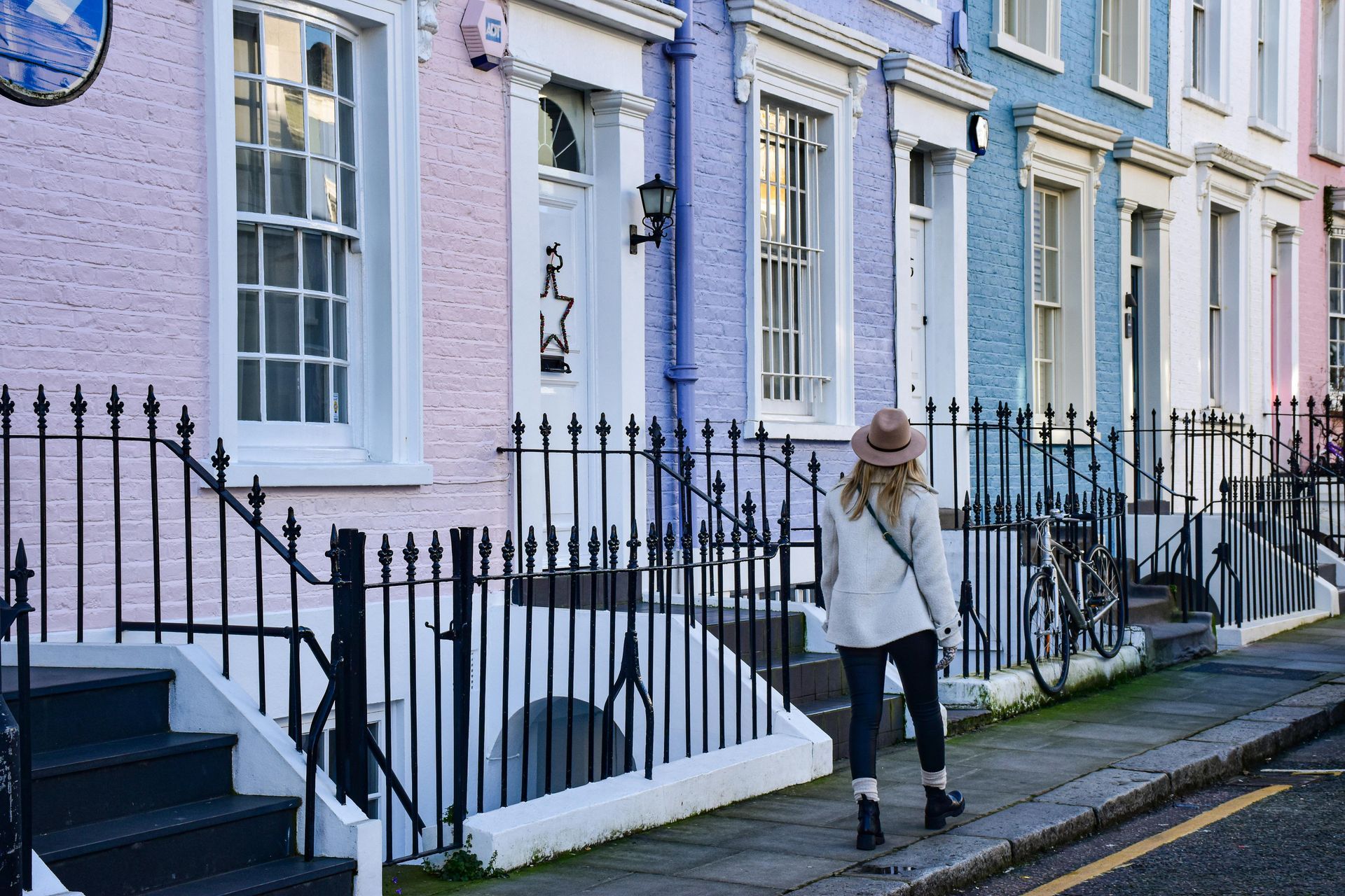 Woman walking past colorful row houses with black fences and stairs.