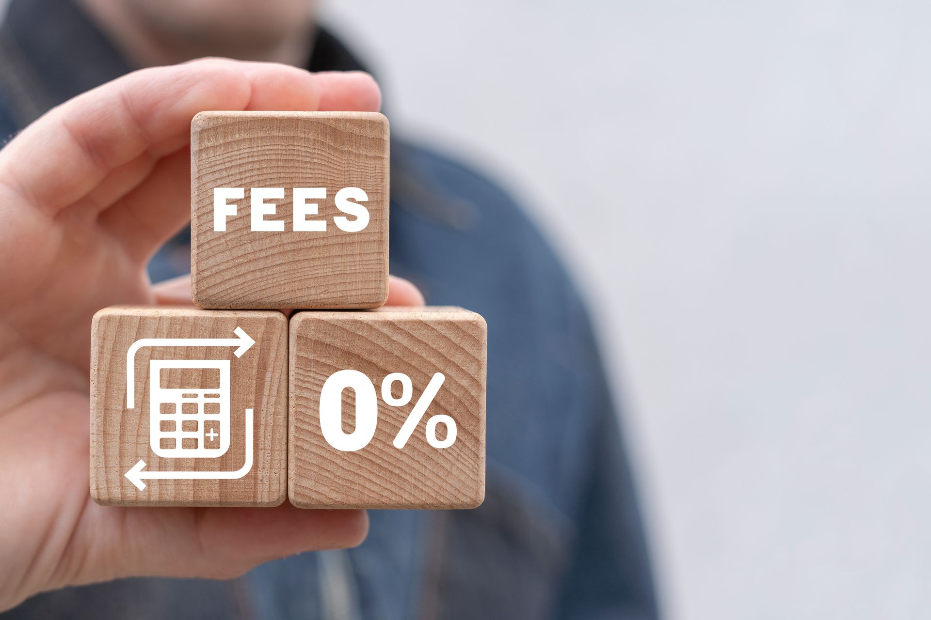 Hand holding wooden blocks labeled “FEES” and “0%” with a calculator icon on a blurred background Hand holding wooden blocks labeled “FEES” and “0%” with a calculator icon on a blurred background