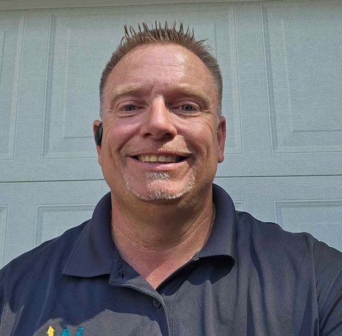 A man in a blue shirt is smiling in front of a garage door.