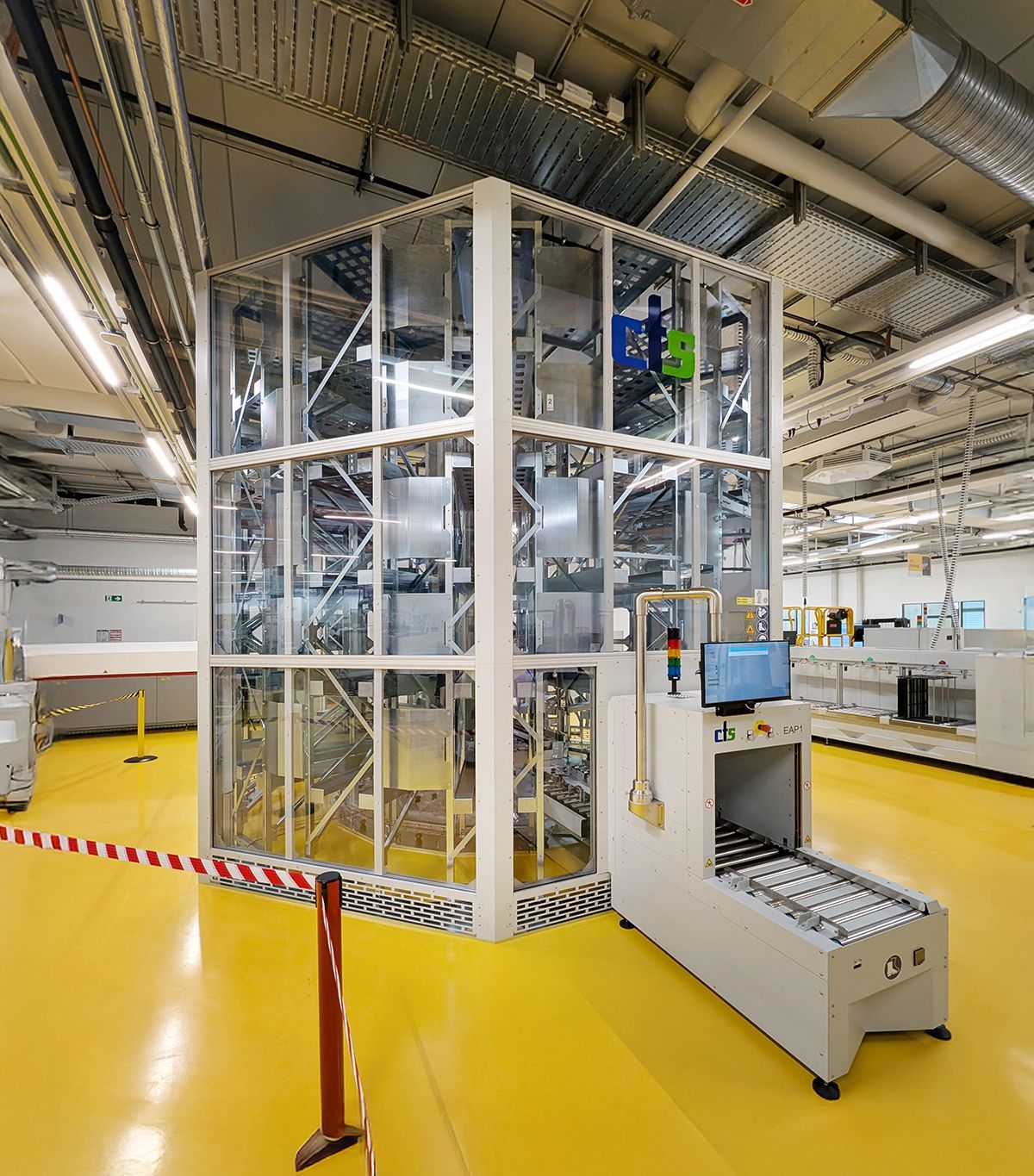 Eine große, transparente Maschine in einer hellen Fabrikhalle mit Förderband und Computer.