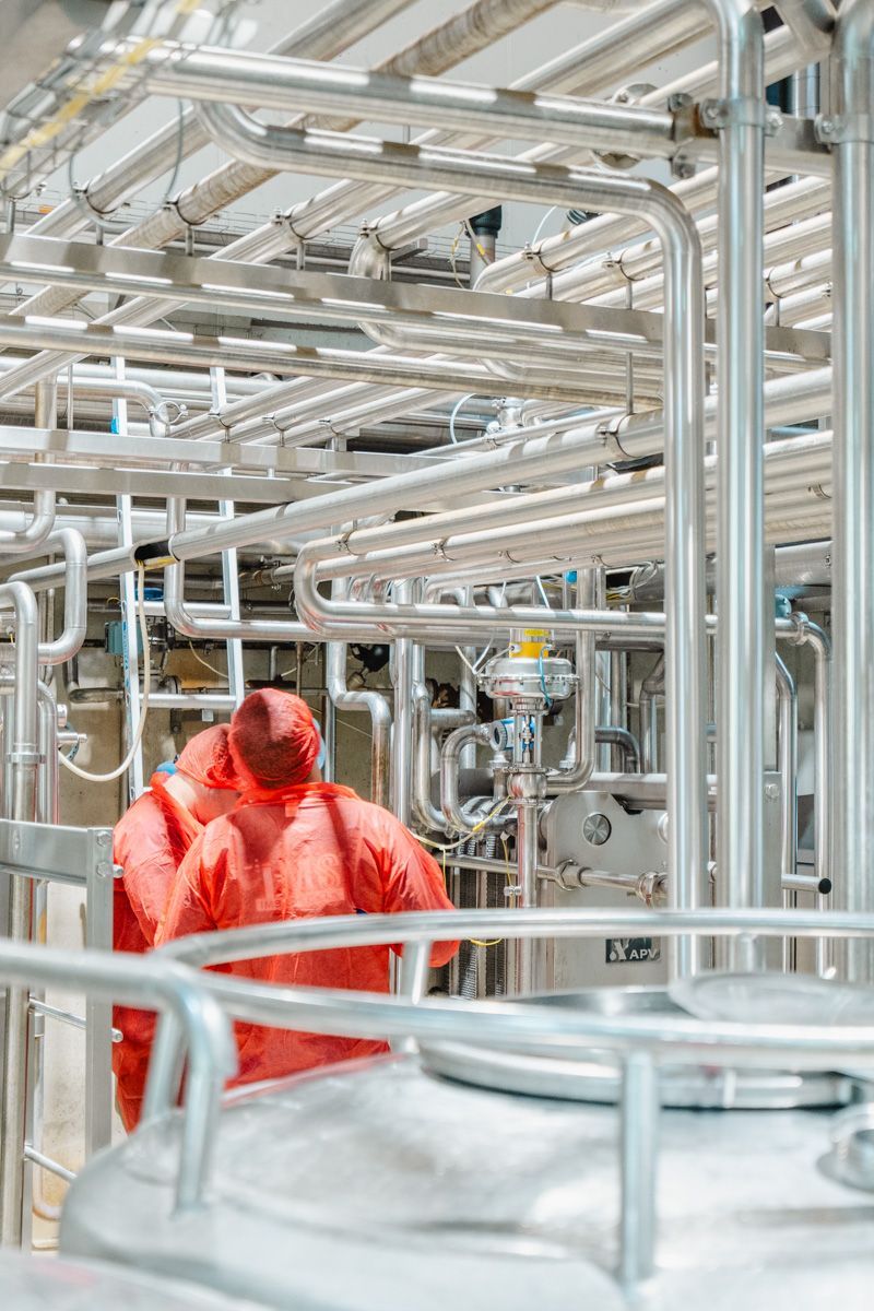 A man in a red suit is standing in a factory surrounded by pipes.