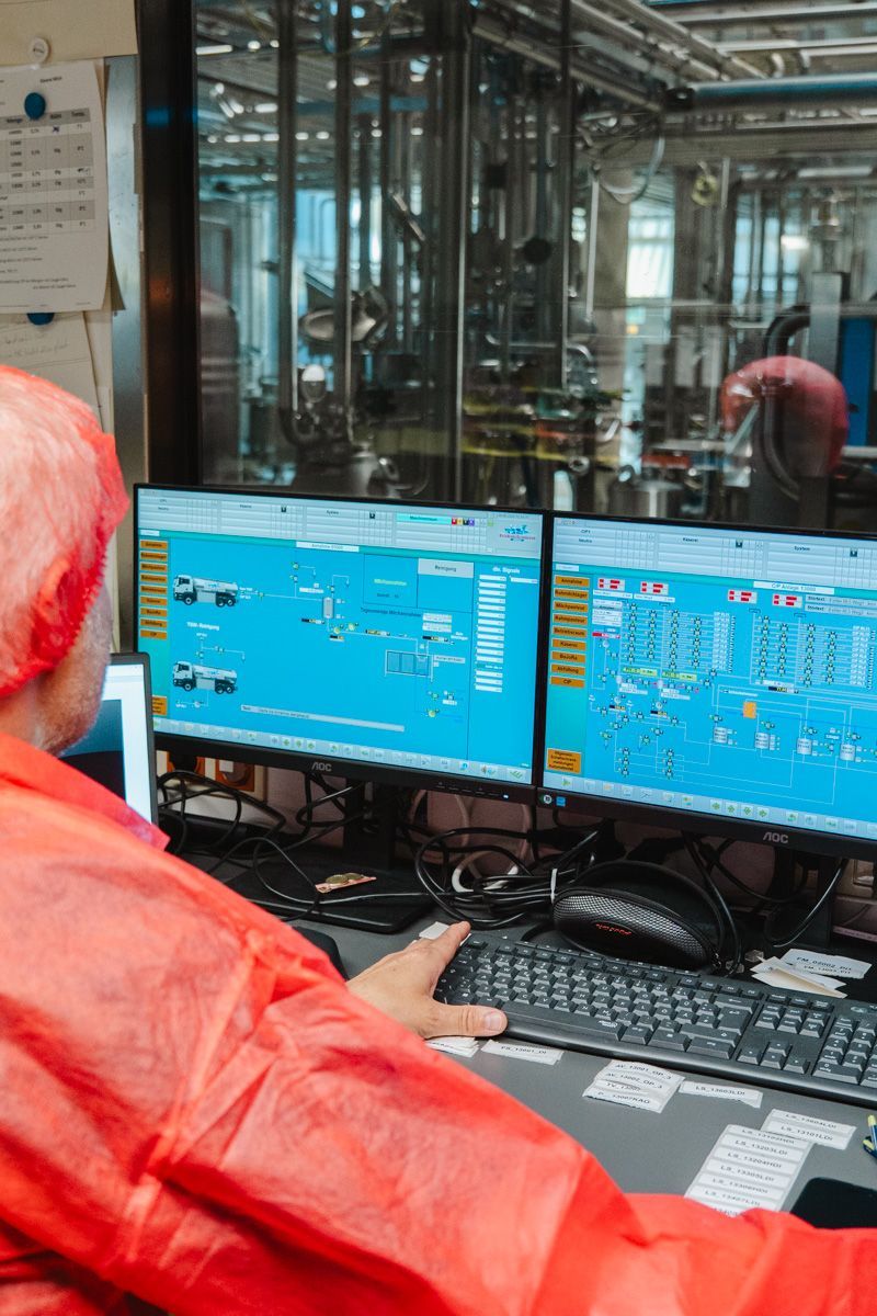 A man in a red coat is sitting in front of two computer monitors.