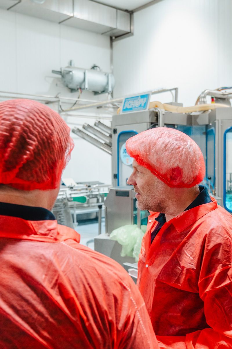 Two men in red coats and red hats are standing next to each other in a factory.