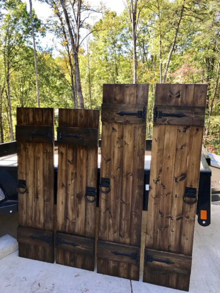Rustic wooden fence panels stacked outdoors on a trailer, with trees in the background.
