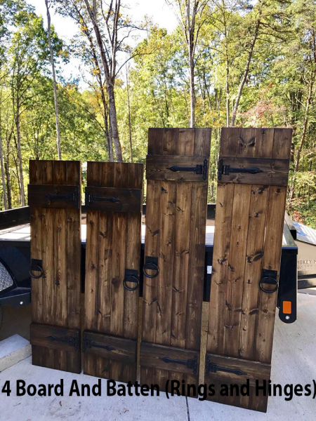 Rustic wooden board-and-batten fence panels with rings and hinges leaning outdoors by trees
