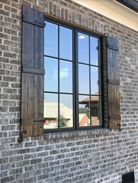 Brick house wall with a black-framed window and dark wooden shutters