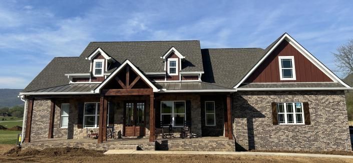 Large stone house with dark roof, dormer windows, and covered front porch under a blue sky