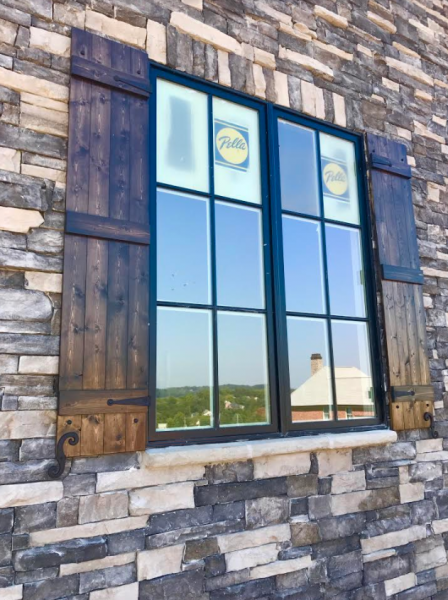 Stone building facade with black-framed windows and rustic blue shutters reflecting the sky