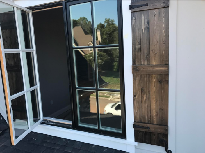 Open balcony door beside a dark window and wooden shutter on a house exterior.