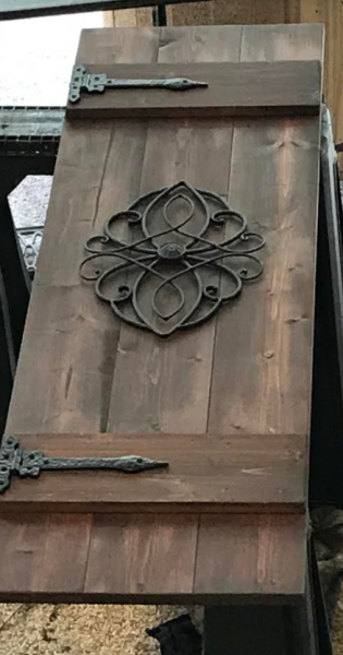Rustic wooden door with ornate black iron hinges and a decorative floral metal centerpiece