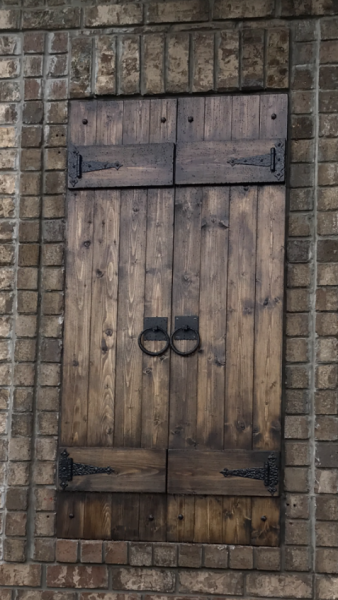 Weathered wooden door with metal hardware set in a brick wall, with a small shuttered opening above.