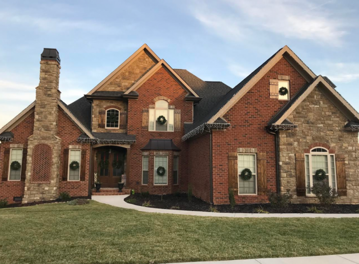 Large red-brick suburban house with multiple gables, arched windows, and a front lawn under a clear sky