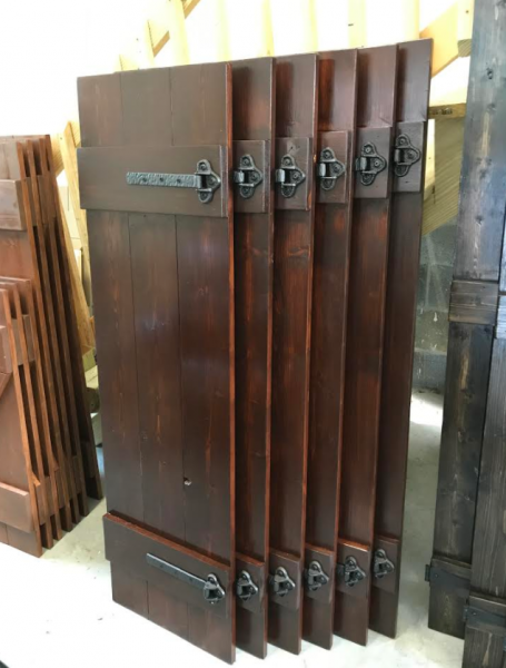Brown wooden window shutters with metal latches, stacked upright in a workshop or storage area