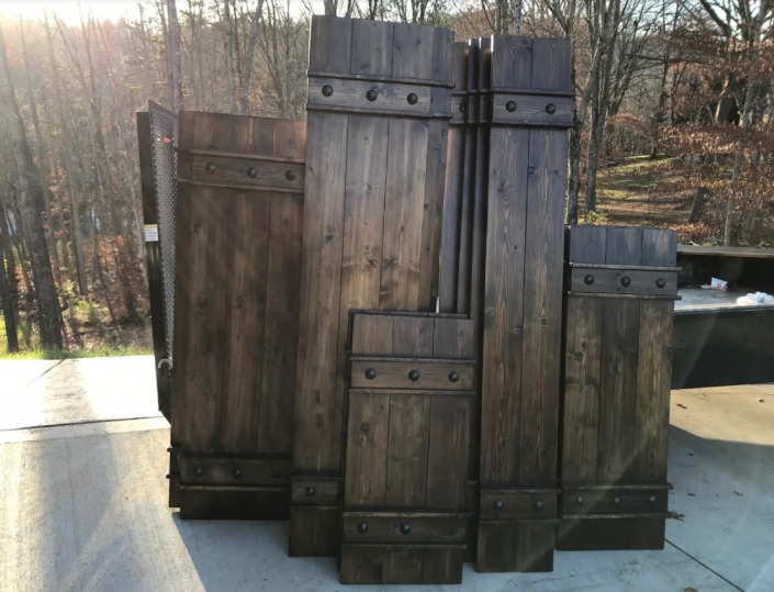 Rustic wooden cabinet or door panels leaning together outdoors on a sunlit deck.