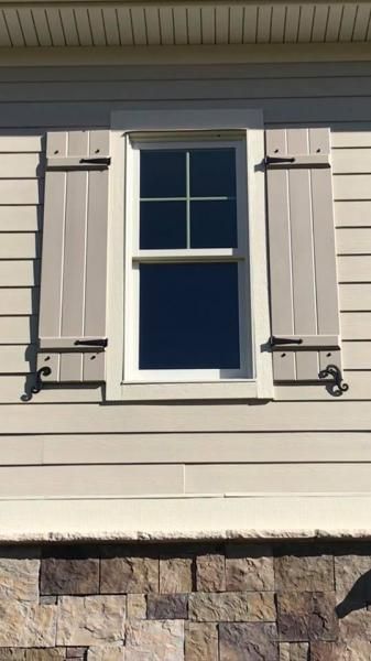 White window with beige shutters on a light-sided house above a stone foundation