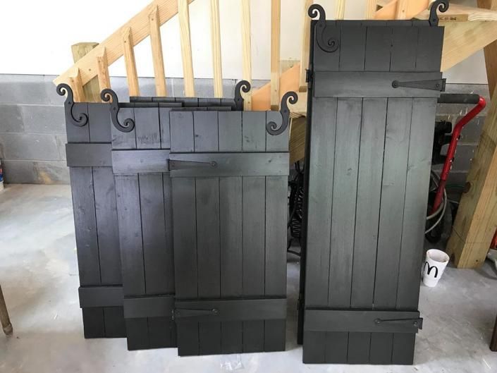 Two tall black wooden shutters with decorative curled tops leaning against a wall in a garage