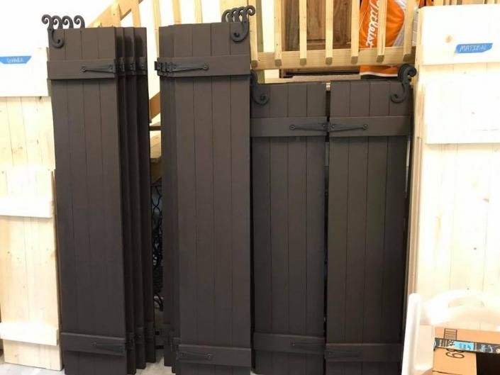 Folded black metal patio gates stacked upright in a storage area, with beige walls and pipes behind them.
