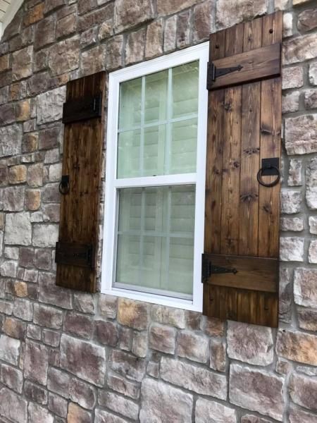 Stone house wall with a white window framed by dark wooden shutters.