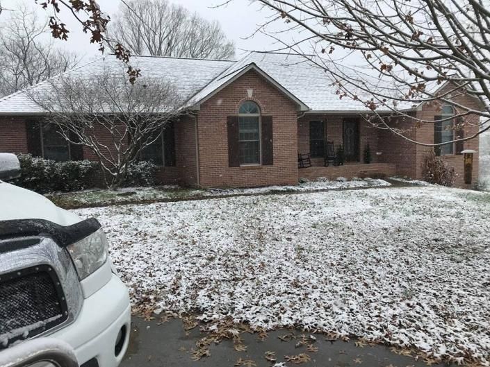Snow-covered suburban brick house with a parked white SUV in the driveway.