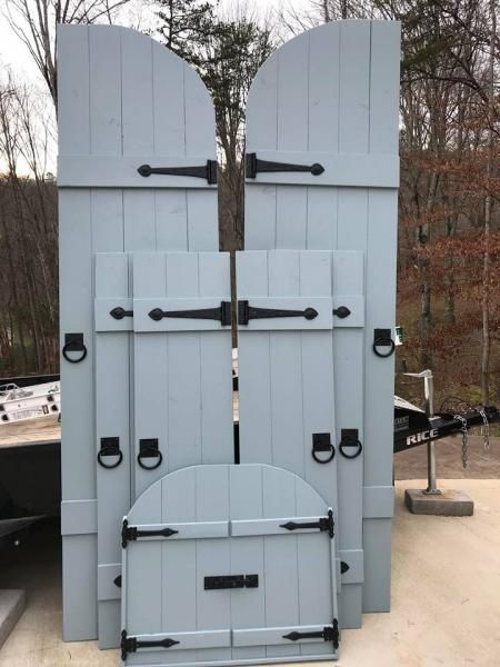 White wooden double doors with black hardware, set outdoors against a wooded background.