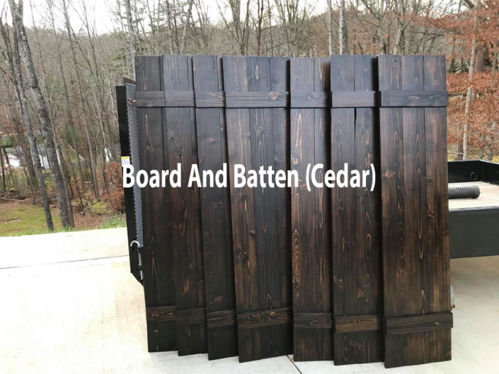 Dark cedar board-and-batten fence panel standing outdoors, with trees in the background.