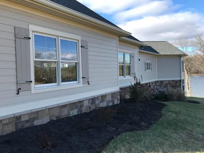 Exterior of a beige house with white-trimmed windows and a dark mulch bed along the foundation.