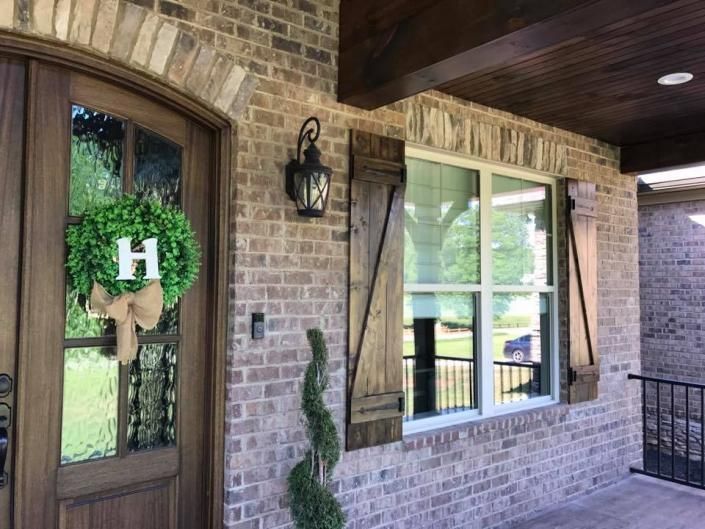Brick porch with wooden door, lantern, window, and green wreath with white H on the left side.