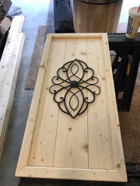 Wooden framed panel on a workbench with a black decorative metal scrollwork centerpiece