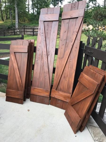 Several wooden shutters and panels leaning against a fence on a patio outdoors.
