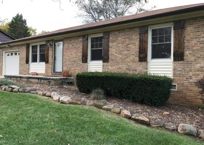 Single-story brick house with white shutters, garage, and stone-bordered front lawn
