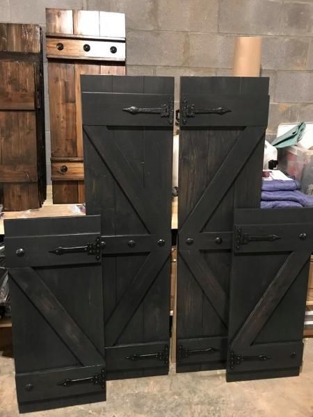 Black wooden cabinets with diagonal cross-brace doors arranged in a stepped stack against a workshop wall.