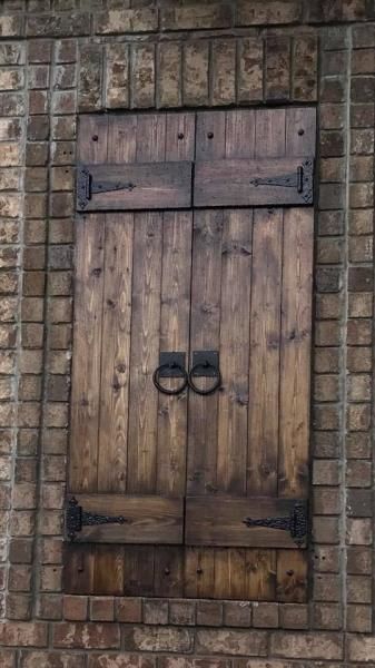 Weathered wooden door with black metal rings, set in a brick wall and sealed with matching shutters above.