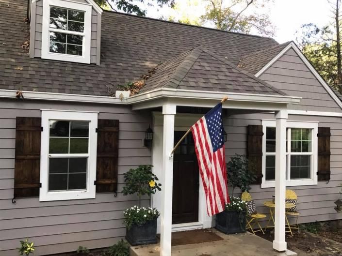 Gray house with white trim and porch, American flag hanging by the front door.