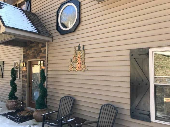 House exterior with tan siding, black shutters, potted topiaries, and a circular window by a patio chair