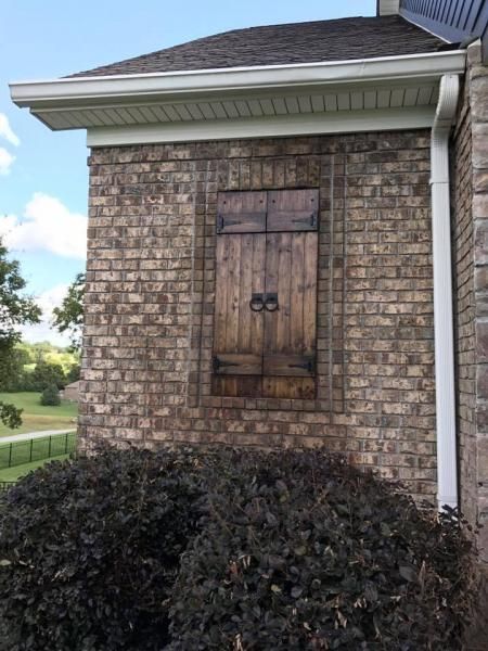 Brick house exterior with a small shuttered window above dark shrubs