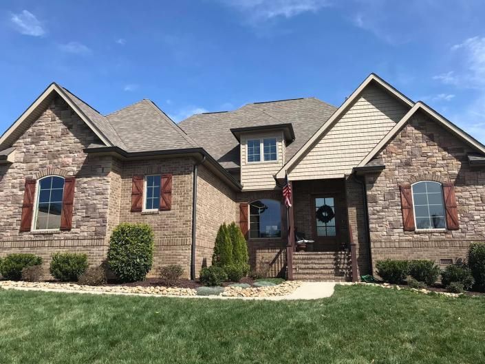 Brick suburban house with gray roof, red shutters, and a front porch under a blue sky