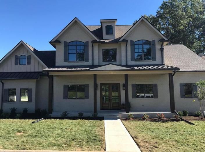 Large two-story suburban house with gray siding, front porch, and central walkway under a clear sky