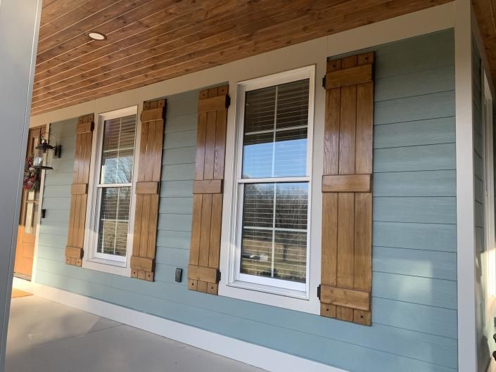 Porch with three windows, white trim, gray siding, and rustic wood shutters under a wood ceiling