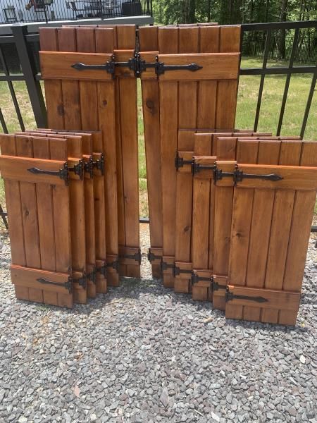 Three wooden gate panels with black metal hinges and latches on gravel, leaning in front of a fence.