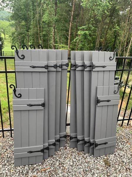 Gray folded outdoor fence panels leaning against a black metal fence on gravel.