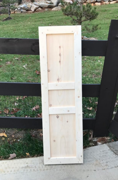 White wooden cabinet door leaning against a black fence outdoors on a concrete path.
