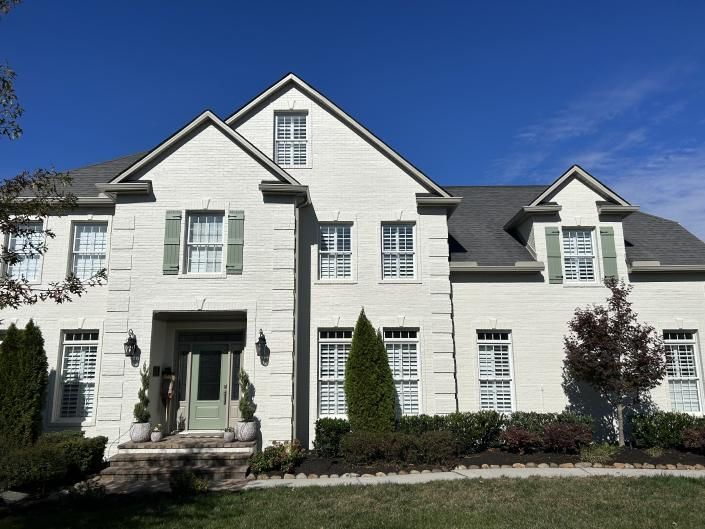 Large white two-story suburban house with dark roof, front porch, and landscaped yard under a blue sky