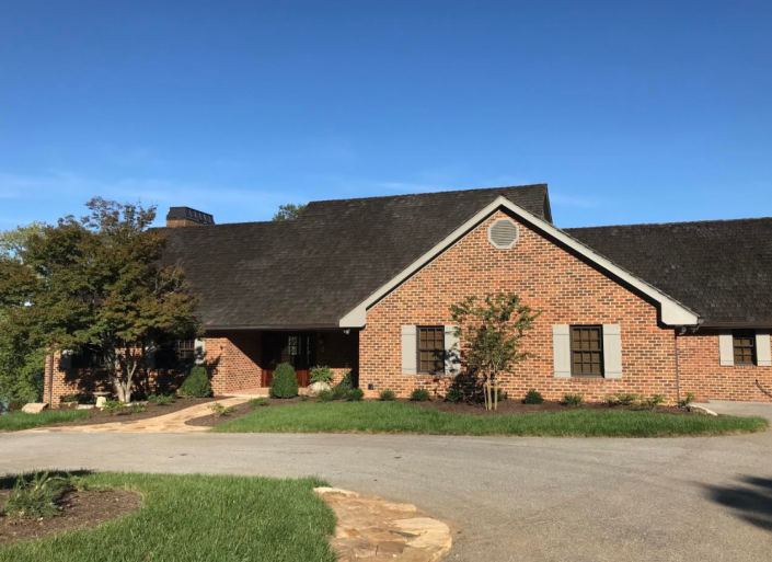 Brick house with a dark roof and front windows, set beside a driveway under a clear blue sky.