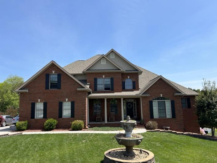 Brick suburban house with a front lawn and decorative fountain under a clear blue sky