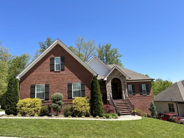 Brick house with arched front porch, green shutters, and landscaped yard under a clear blue sky