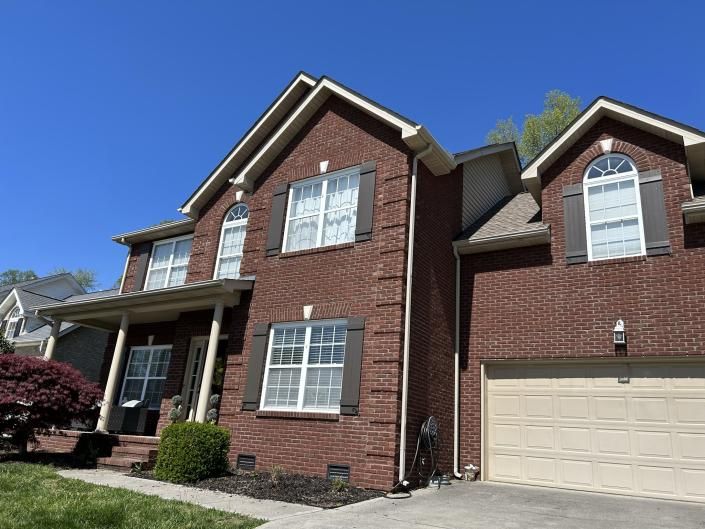Two-story brick suburban house with a front porch, garage, and clear blue sky