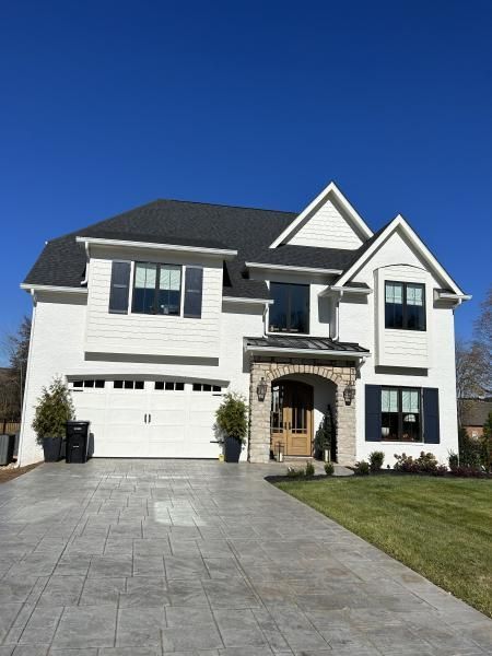Large two-story white house with dark roof, stone entry, and wide driveway under a clear blue sky