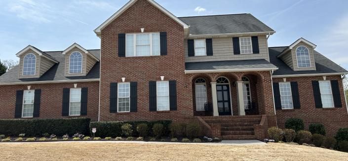 Large two-story brick house with gray roof, white trim, and front steps in a suburban yard