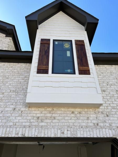 White dormer window with dark shutters on a brick house against a blue sky